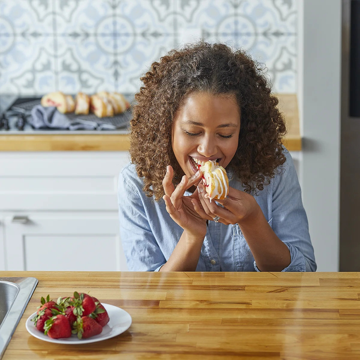 Woman enjoying a strawberry cream cheese Butter Braid pastry in a bright kitchen